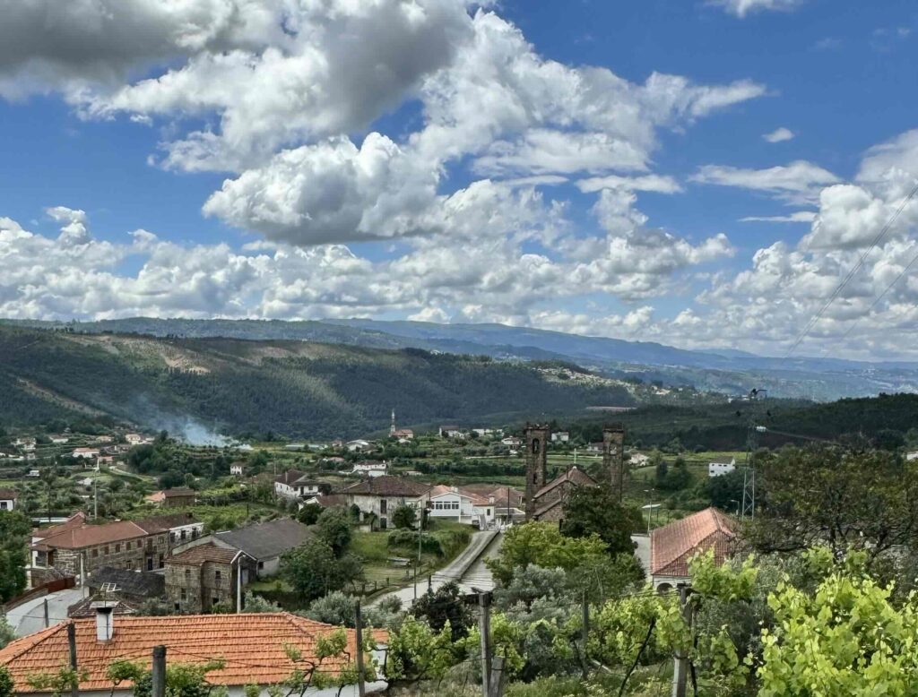 View of the valley with buildings and lush green mountains and blue skies with white puffy clouds. 