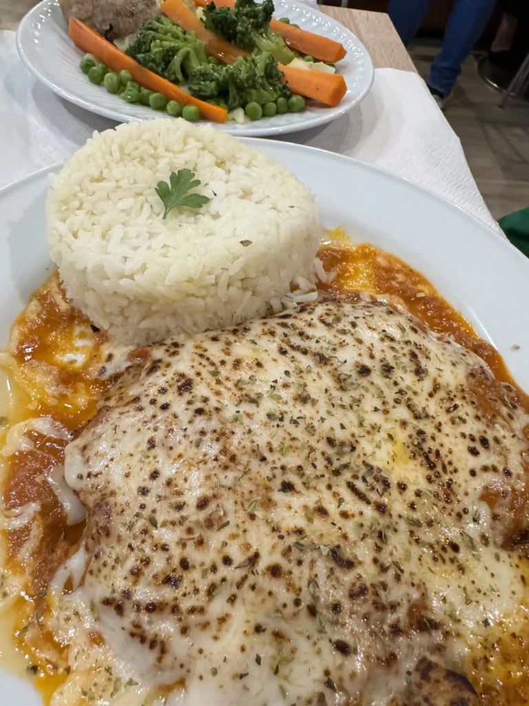 Bella Braga Chicken Parm with white rise and a side of steamed carrots and peas.